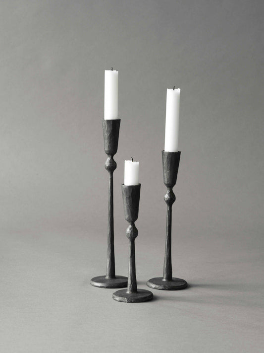 Set of three black candle holders with white candles on a gray background