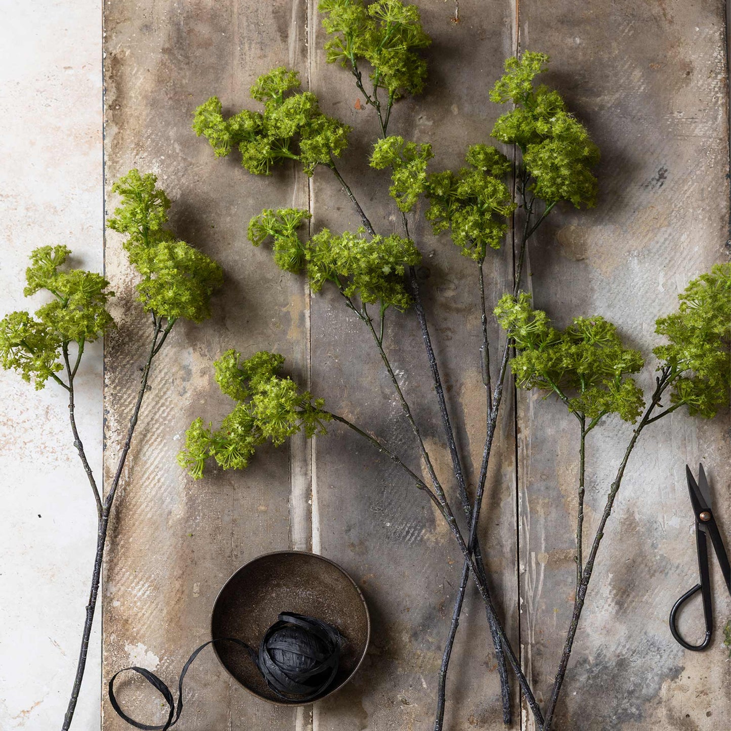 Green artificial flowers on a textured surface with a pair of scissors.
