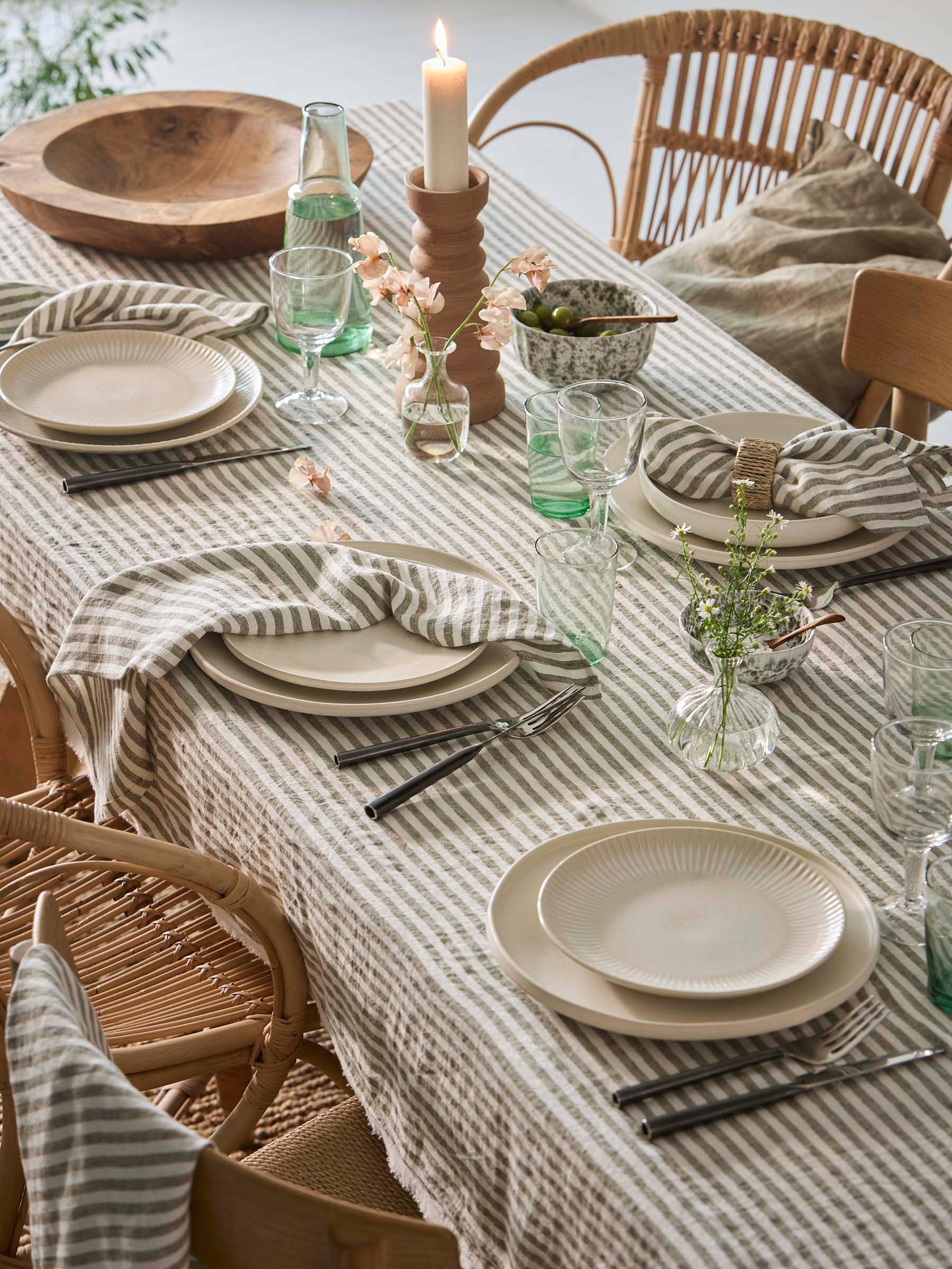 Dining table set with plates, glasses, and candles on a striped tablecloth.