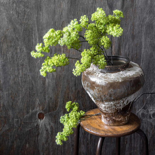 Decorative vase with green branches on a wooden stool against a dark textured wall