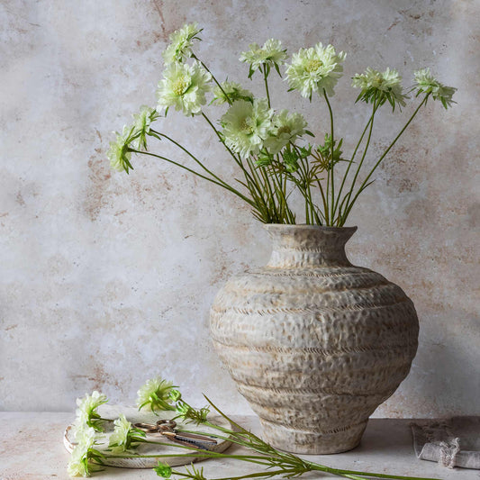 Decorative vase with green flowers against a textured wall