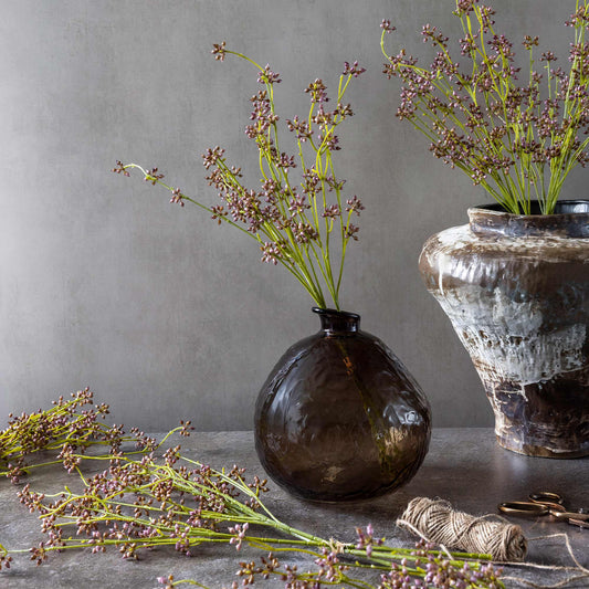 Two vases with dried plants on a gray surface against a gray wall