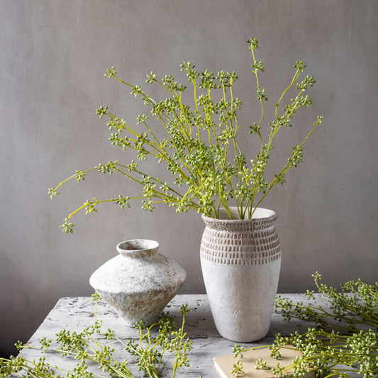 Two textured vases with greenery on a wooden surface against a gray background
