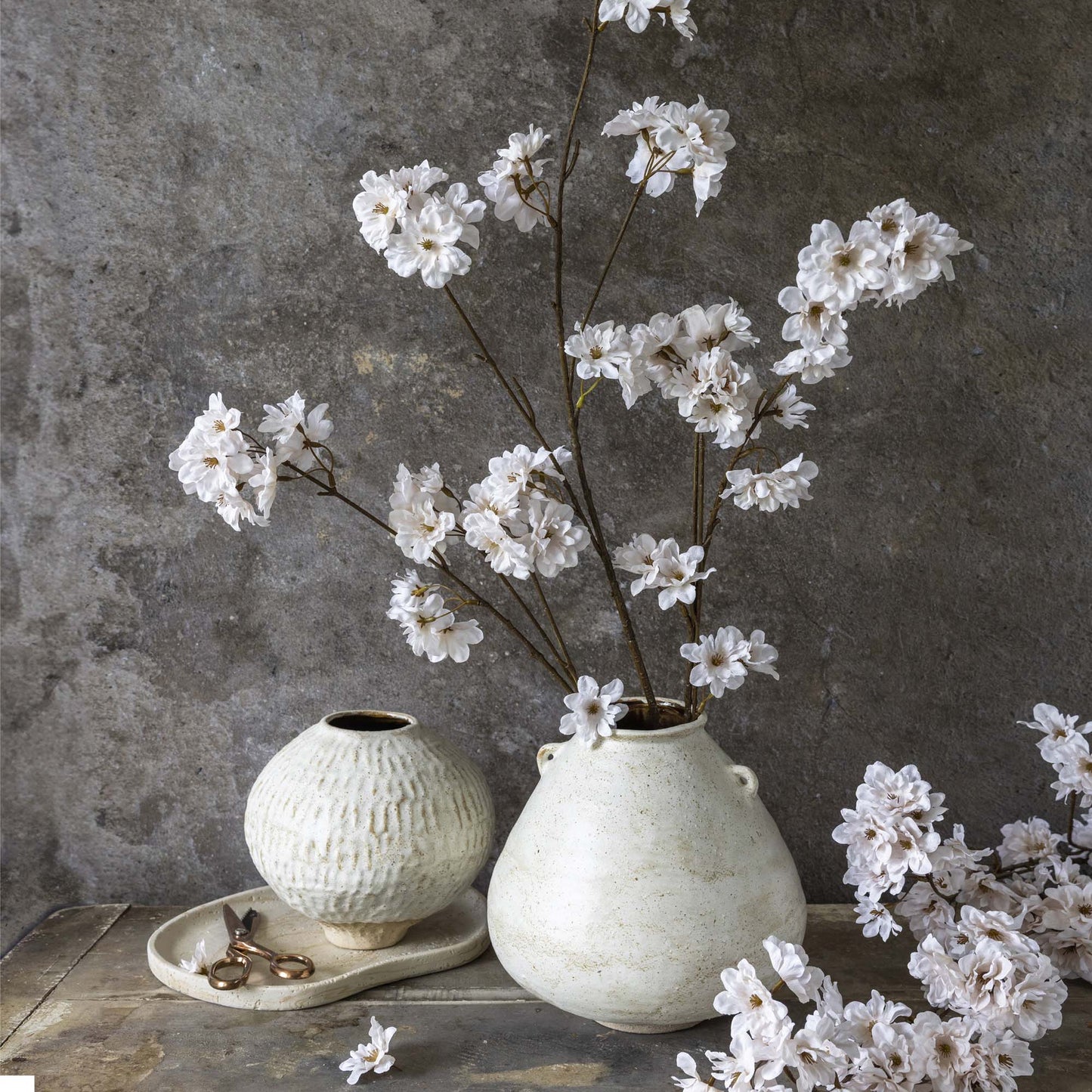 White flowers in a textured ceramic vase against a gray concrete wall.