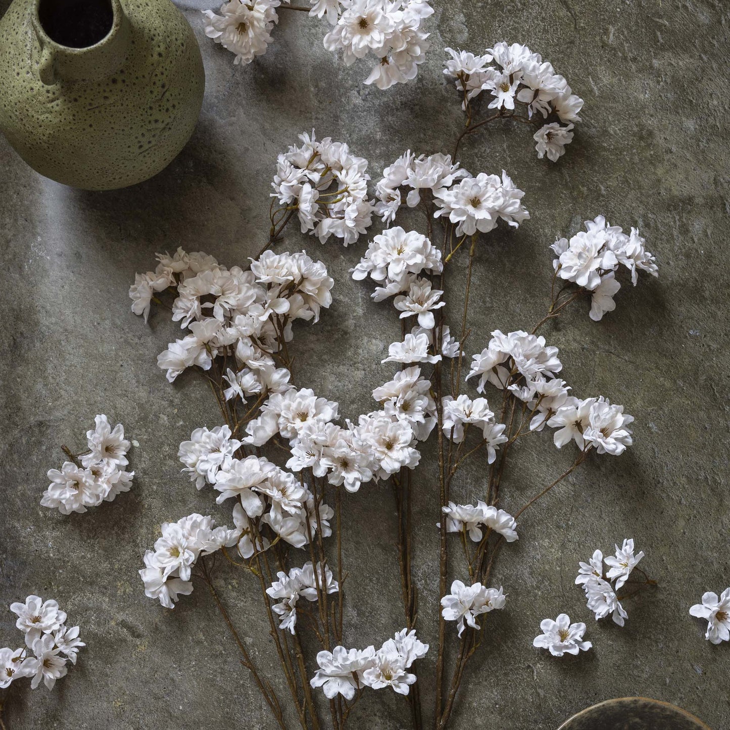 White flowers on a textured stone surface with a green ceramic vase.