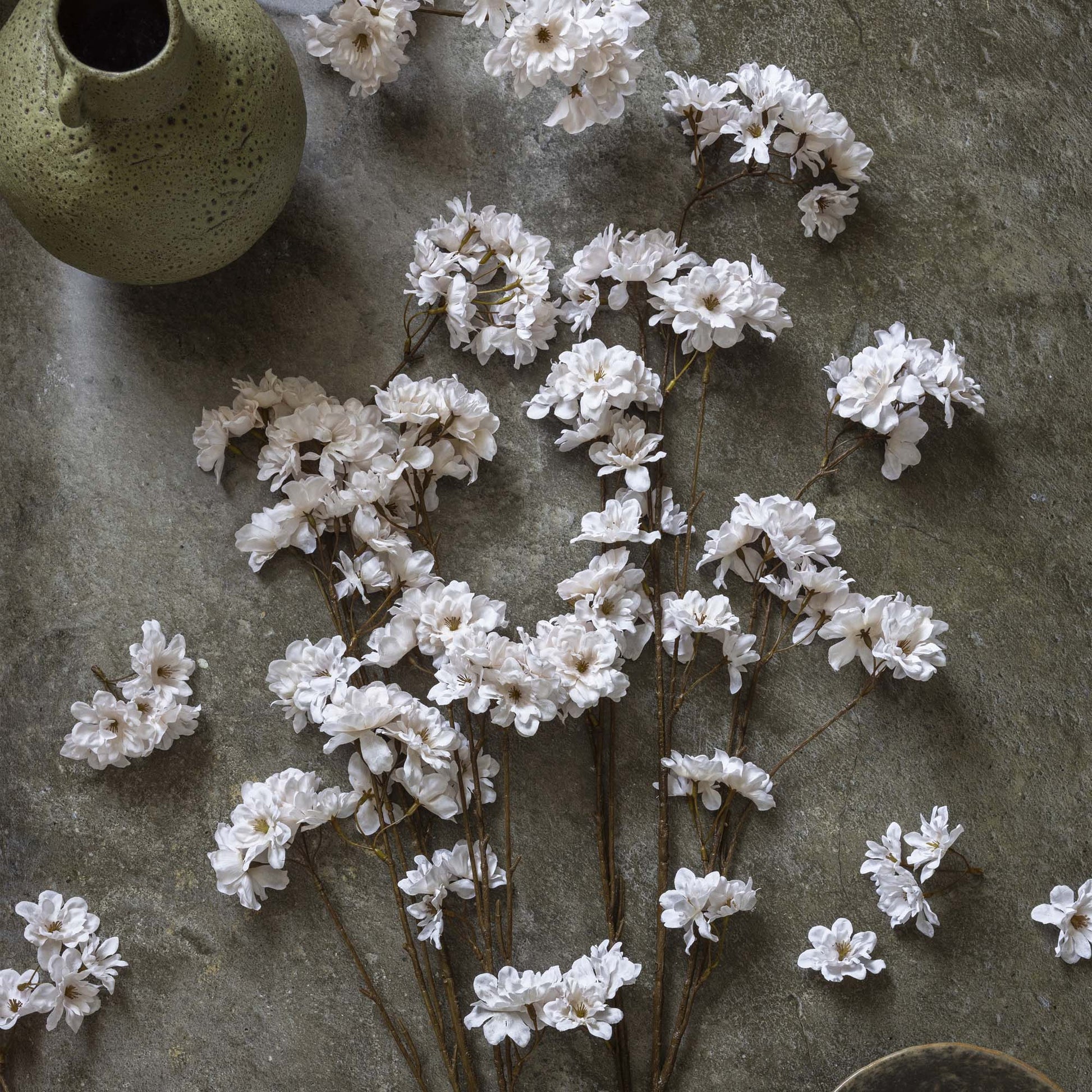White flowers on a textured stone surface with a green ceramic vase.