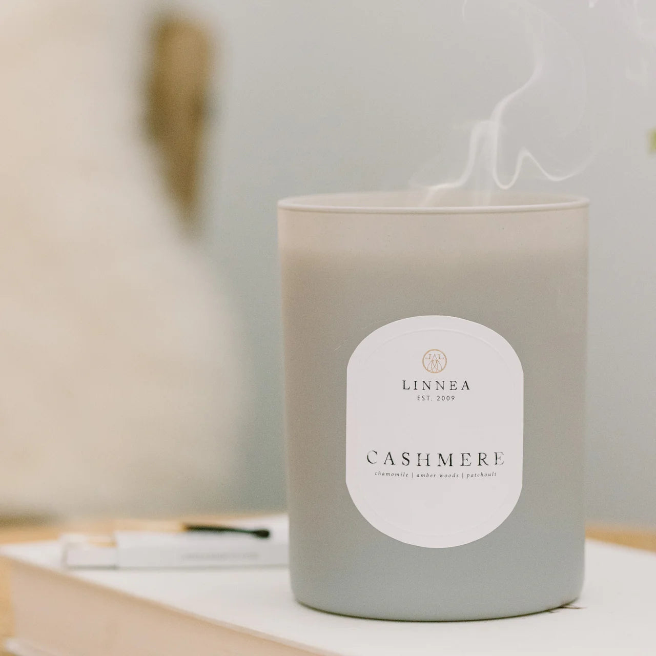 Candle labeled 'Cashmere' by Linnea on a table with a blurred background