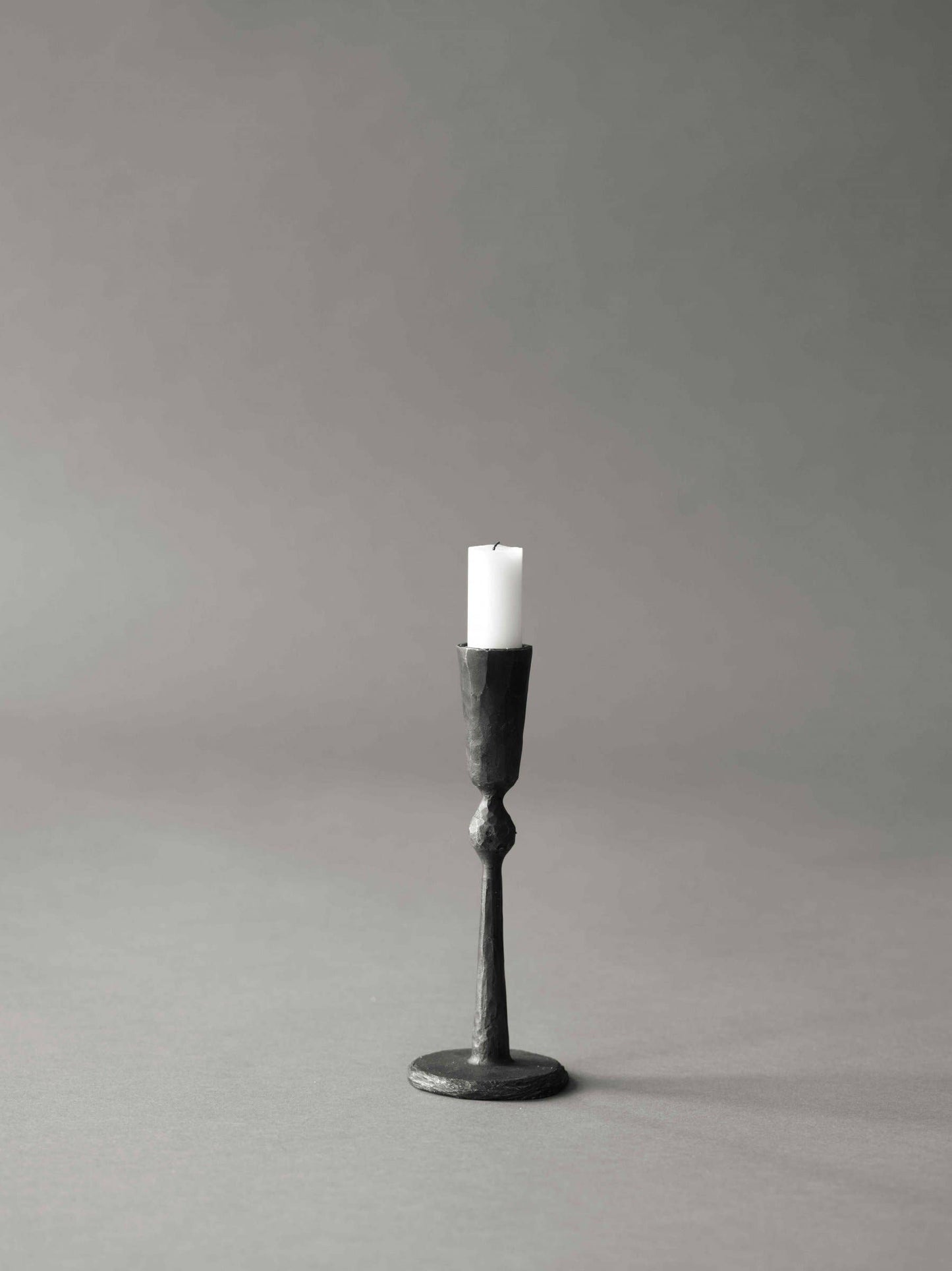 Black candle holder with a white candle on a gray background