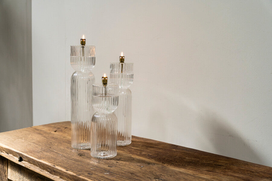 Set of three clear glass oil lamps on a wooden surface with a plain background